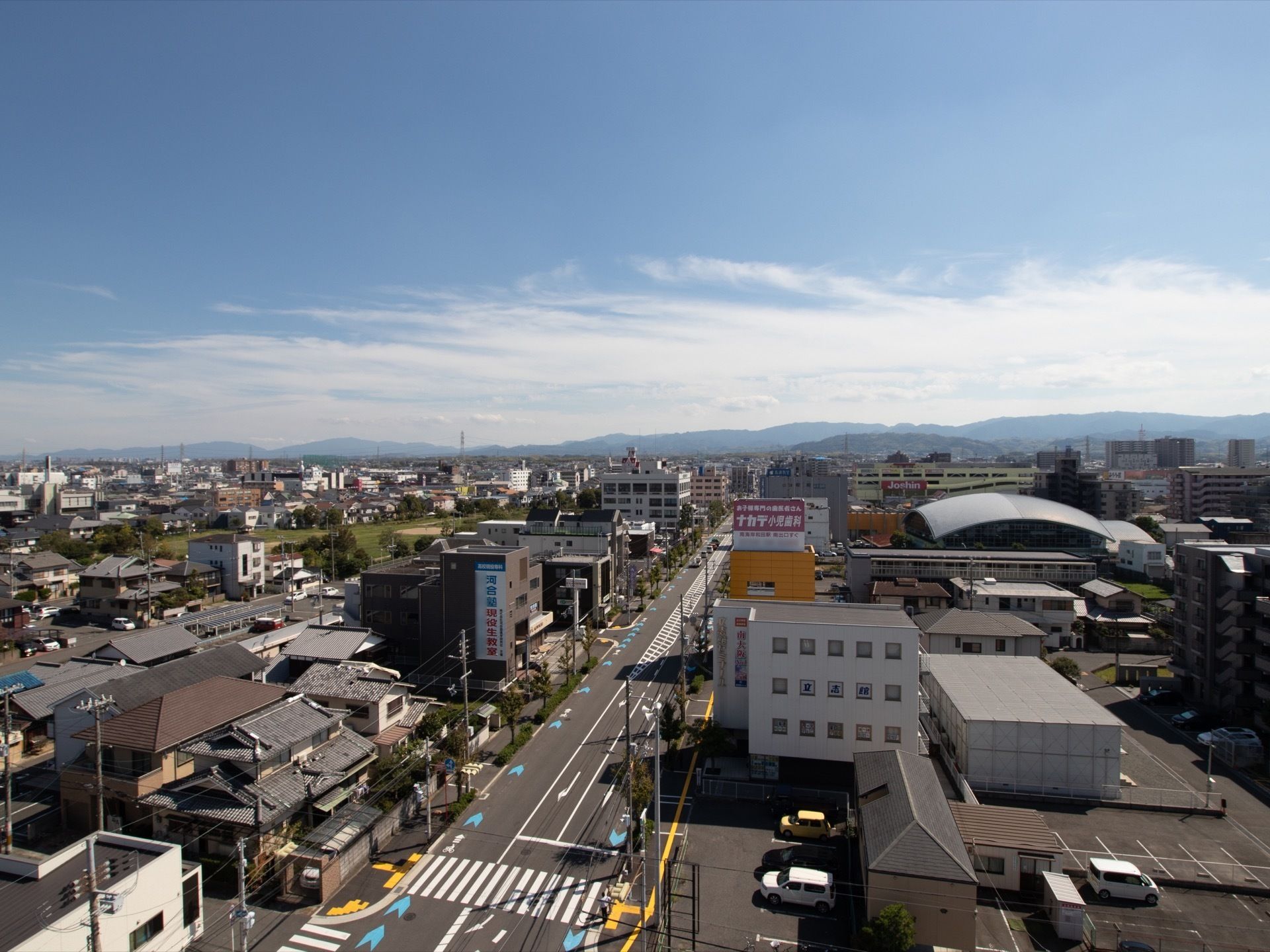 高い位置から見た街の風景。大きな道路や、さまざまな住宅、ビル、ショッピングセンターなどが並んでいるのが見える。