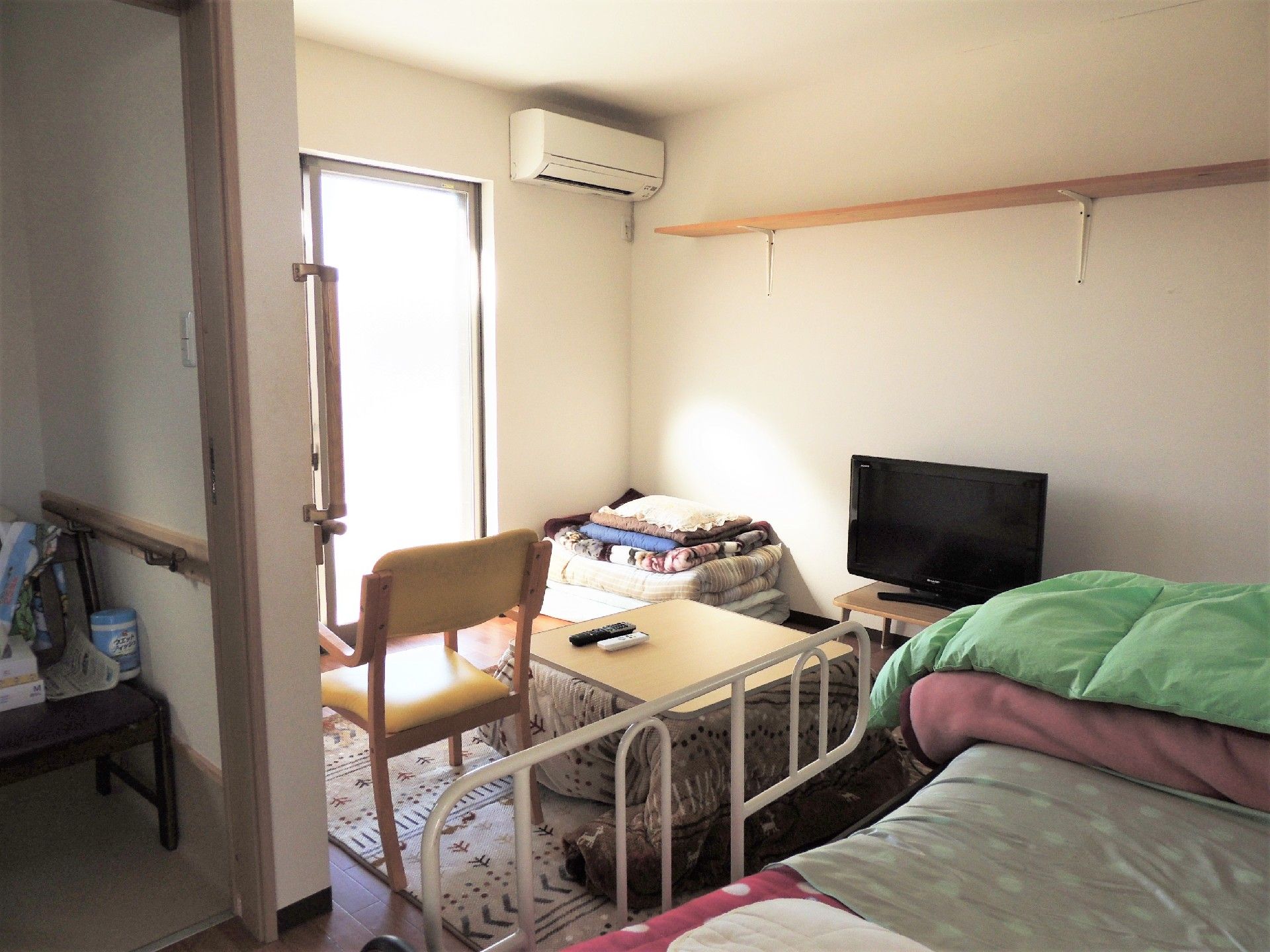 エアコンとベッドが置いてある施設内の部屋の様子。テレビが置いてあるのが見えている写真