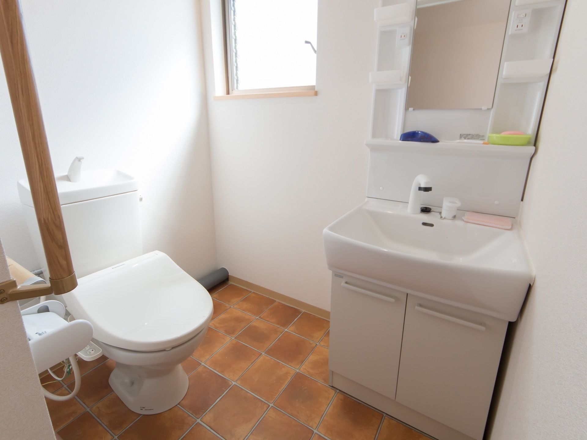 トイレの床には茶色いタイル柄のクッションフロアが敷かれている。シャワー付きの洗面台も設置されている。
