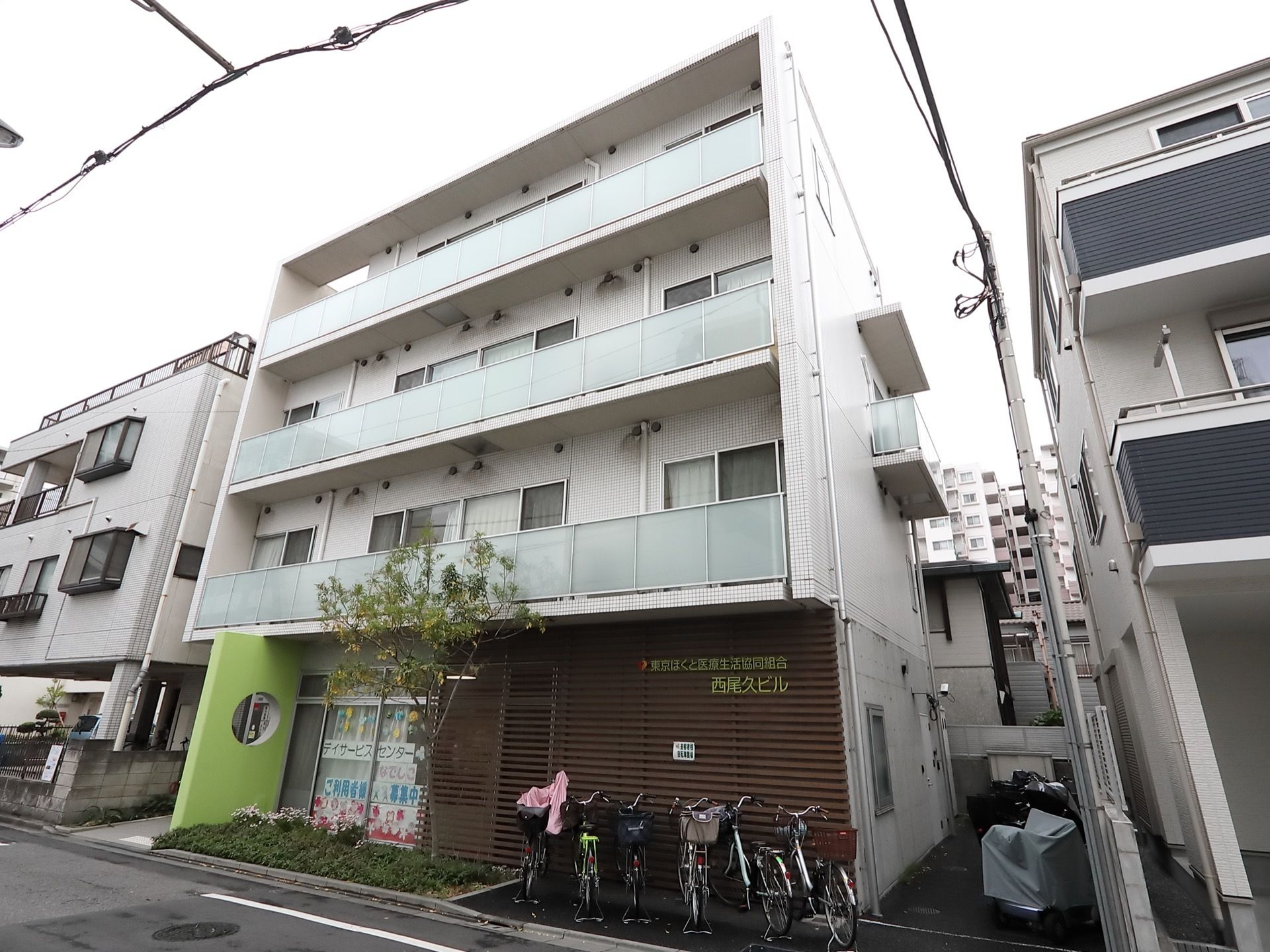 施設はグレー色の外壁になっており４階建ての建物である。建物の前には駐輪場が設置されており、自転車が停まっている。