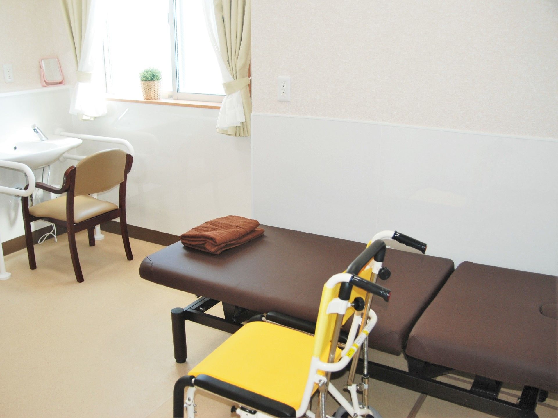 一人用の小さな館員ベッドと車いす、手すり付きの洗面台がある小さな部屋の様子