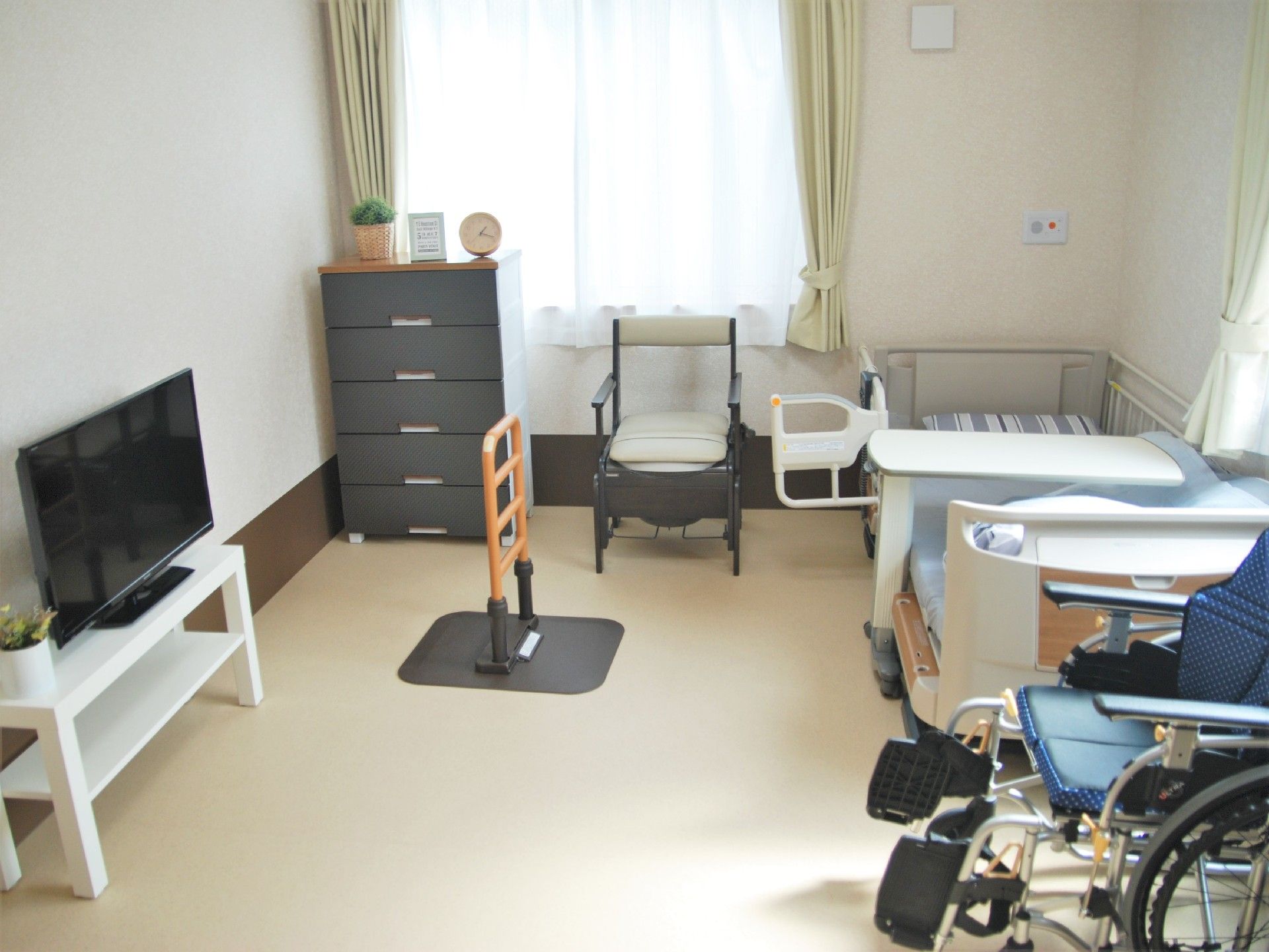 窓がある小さな部屋の様子。手前に車いす、横にテレビとベッドなど生活用品がある