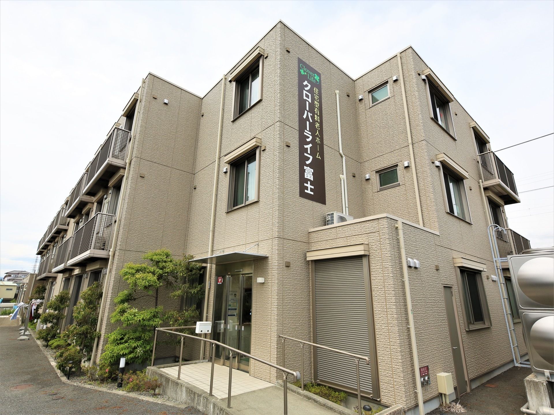 正面玄関付近から見上げた建物外観。エアコン室外機用のカゴが、各居室窓の外側に取りつけられているのが見える。