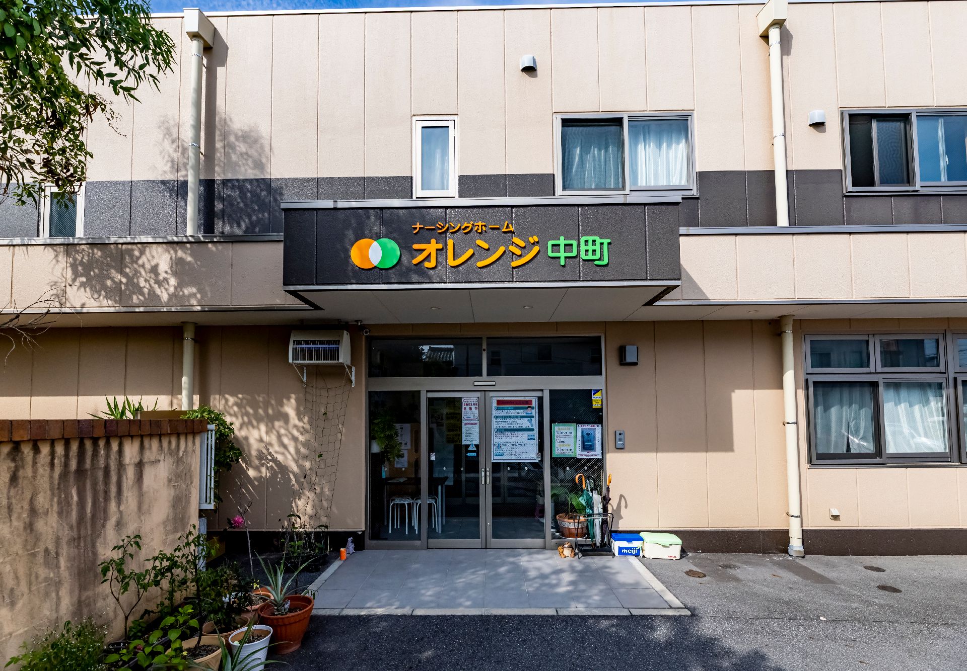 木製のテーブルを囲んで笑顔で話しているピンクのポロシャツを着た女性スタッフと眼鏡をかけた高齢女性。