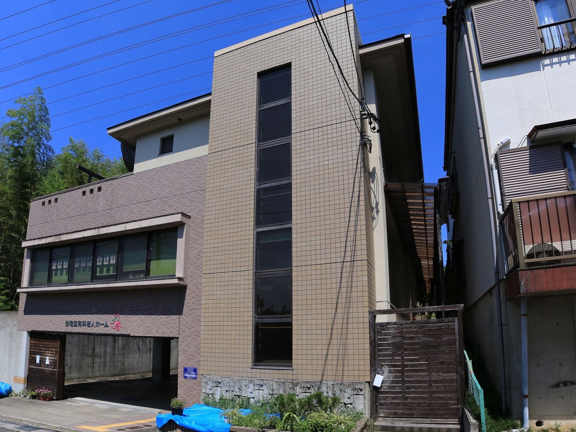 道路に面した日当たりのよい場所に建っている施設である。隣の建物との境界付近にはウッドフェンスが建てられている。