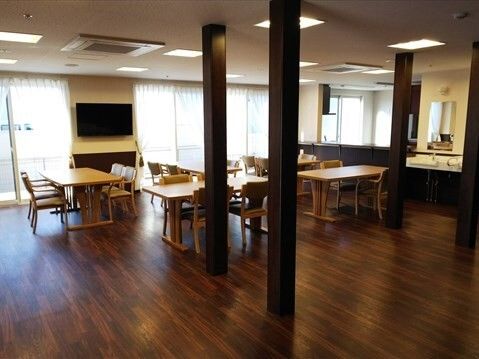 ダークブラウンのフロアには4人掛けのダイニングテーブルが並び、壁には壁掛けテレビが付き、大きな窓が付いている。