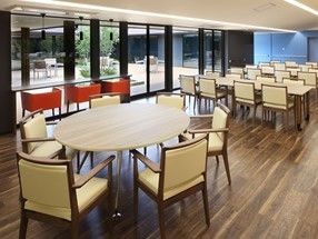 円形のテーブルや長方形のテーブルが並んだ食堂。大きな窓の外にはウッドデッキが見える。