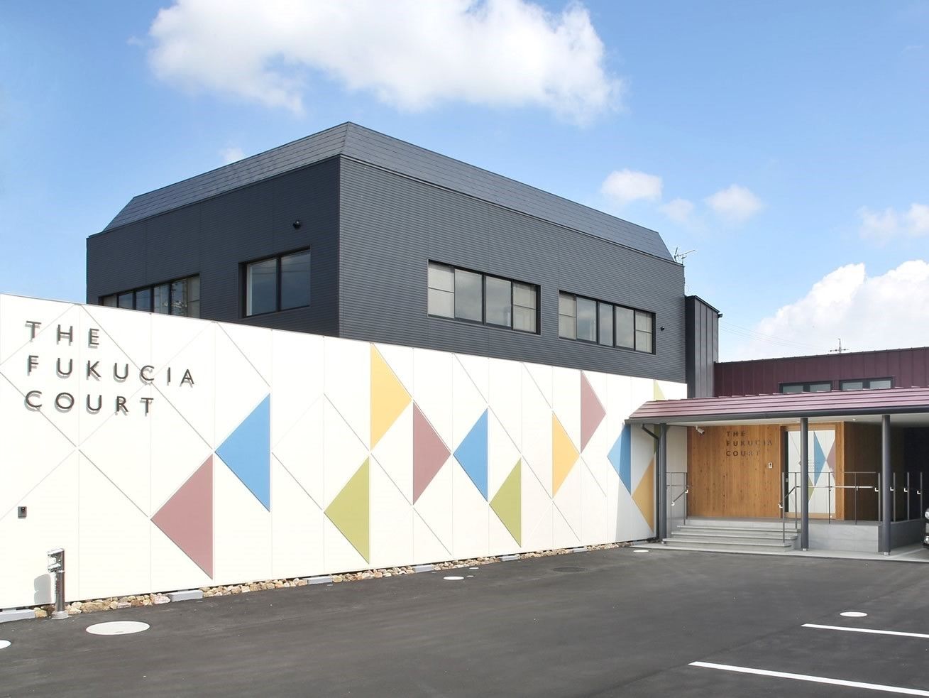 黒い2階建て他の建物の前にはカラフルな模様が描かれた白い壁があり、玄関には屋根がある。