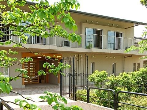 ベージュ系の和風の建物の周りには緑が多く、２階部分にはベランダが付き、出入り口にも段差がない。
