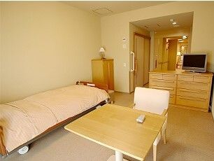 居室にはベッドやタンス、テーブルやいすなどの家具やテレビなどの家電もあり、壁には手すりが付いている。