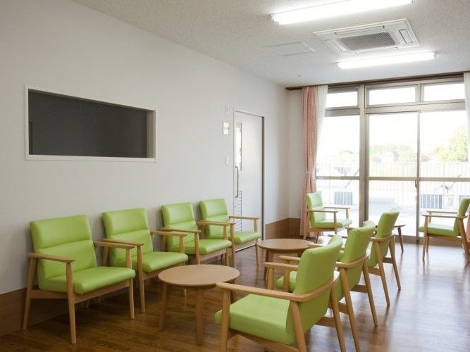 大きな窓が付き明るい雰囲気。緑の椅子と丸テーブルが複数組並んでいる。