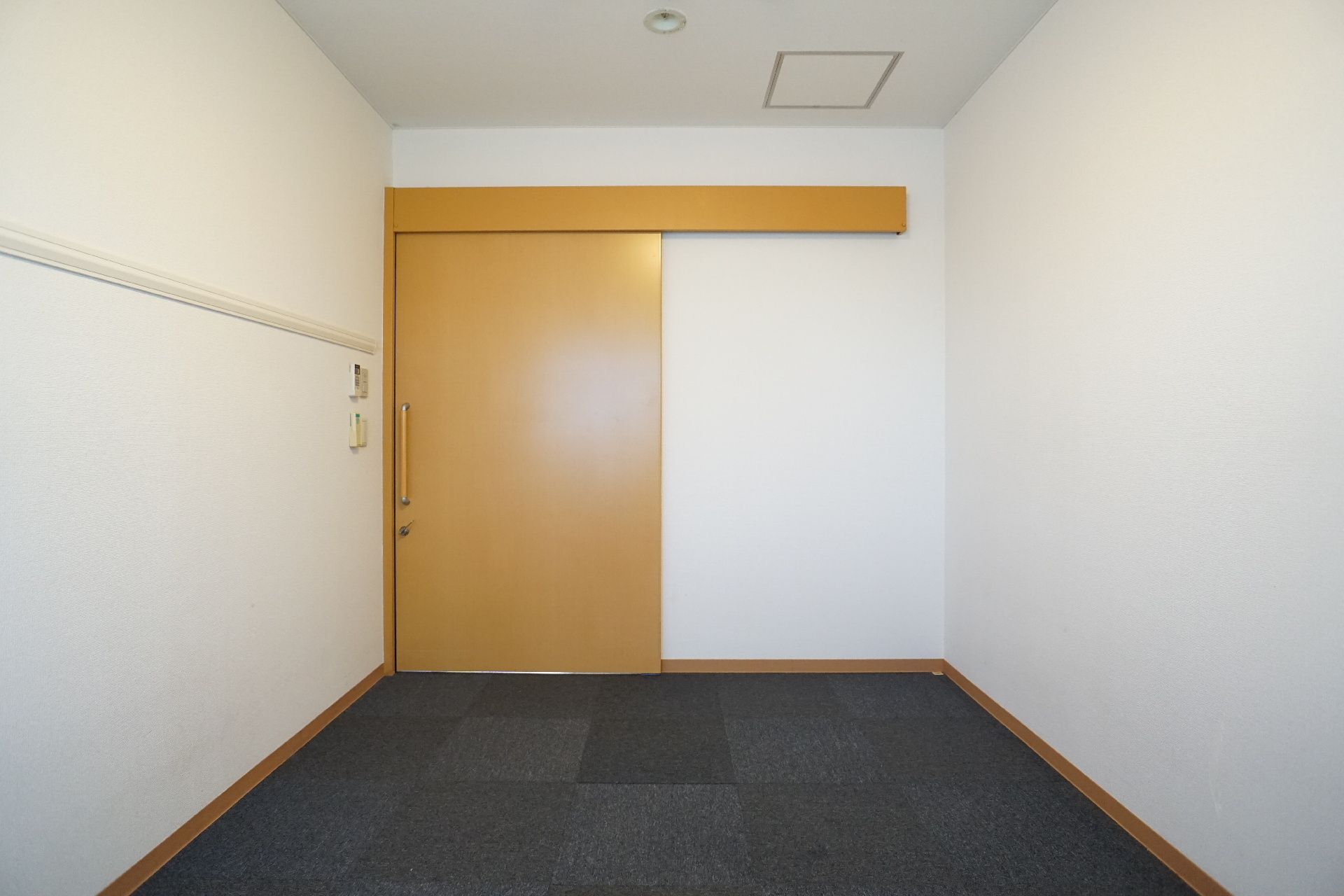何も置かれていない白い壁に木製のスライド式ドアがある部屋