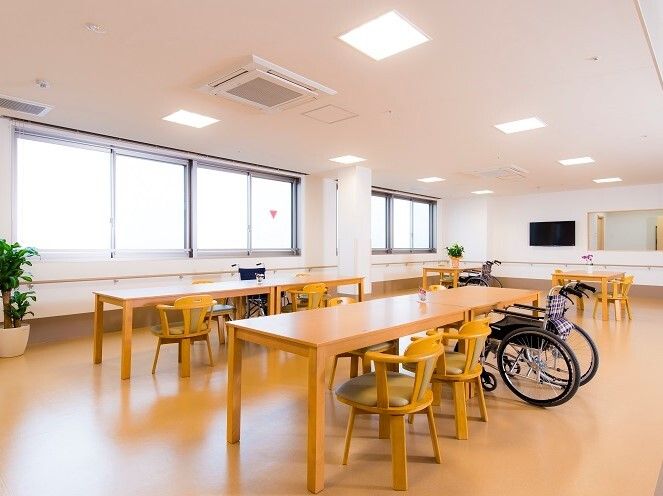 回転いすや車いすがセットされたテーブルが置かれたリビングダイニングには観葉植物やテレビもある。