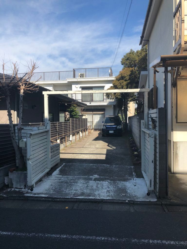 青い空の下に建っている白い2階建ての建物が奥にあり、そこに続く一本道が道路から続いている。