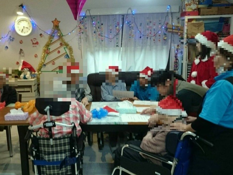 クリスマスの飾りつけがされた部屋でサンタ帽をかぶって歌を歌っている高齢者たちとスタッフ。