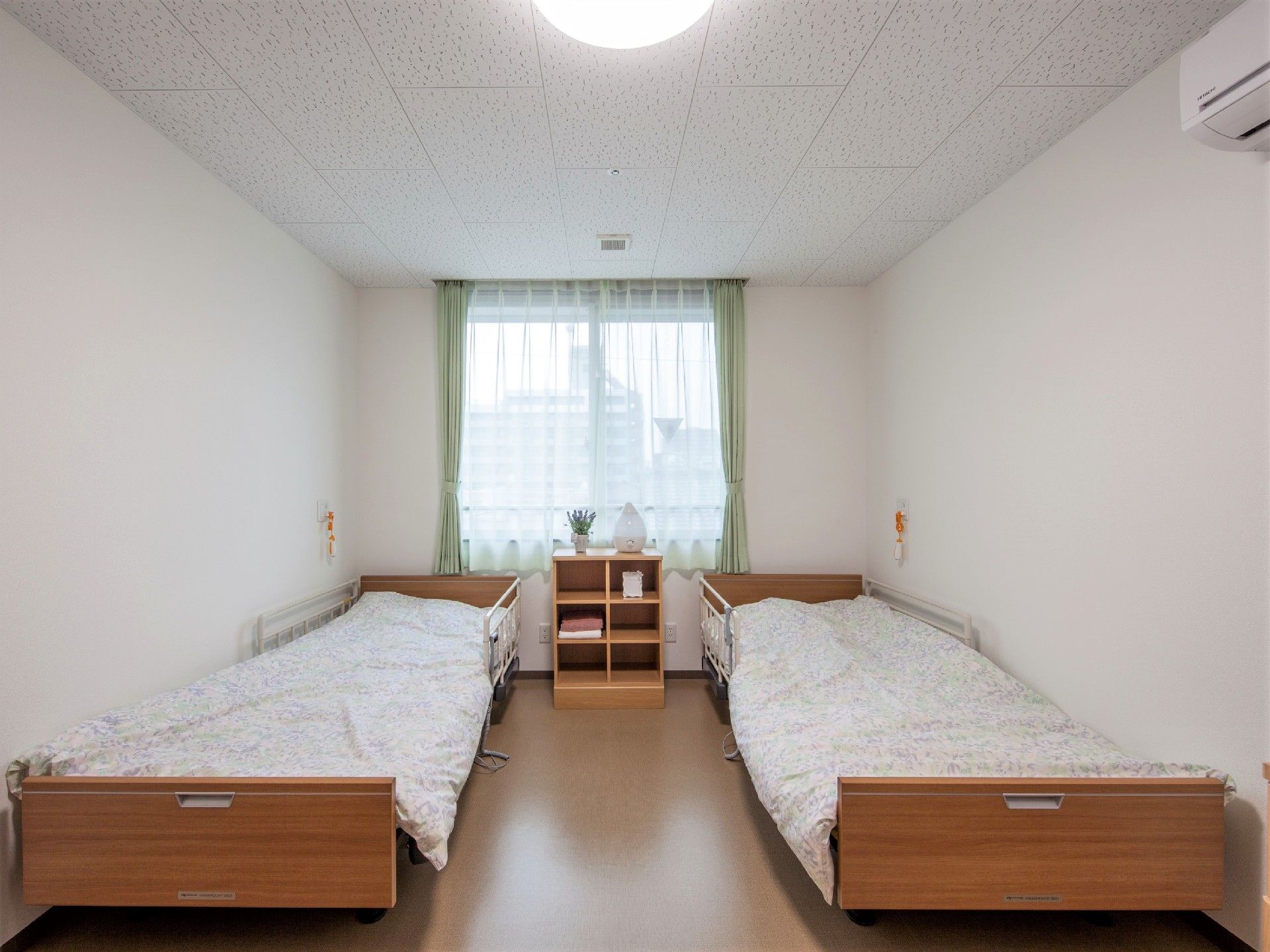 二つのベッドが設置された夫婦用の部屋。各ベッドには寝具がセットされ、窓にはカーテンもある。