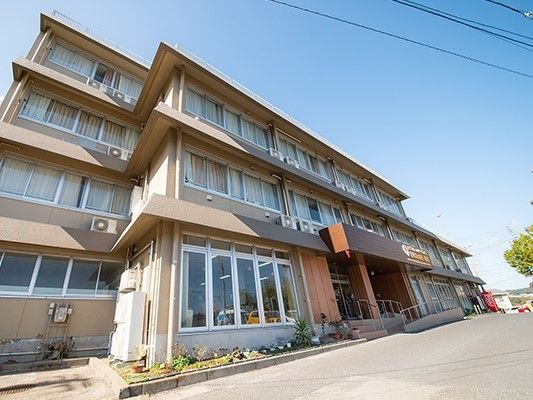 ３階建ての学校のような雰囲気の建物。手前に駐車場がある様子