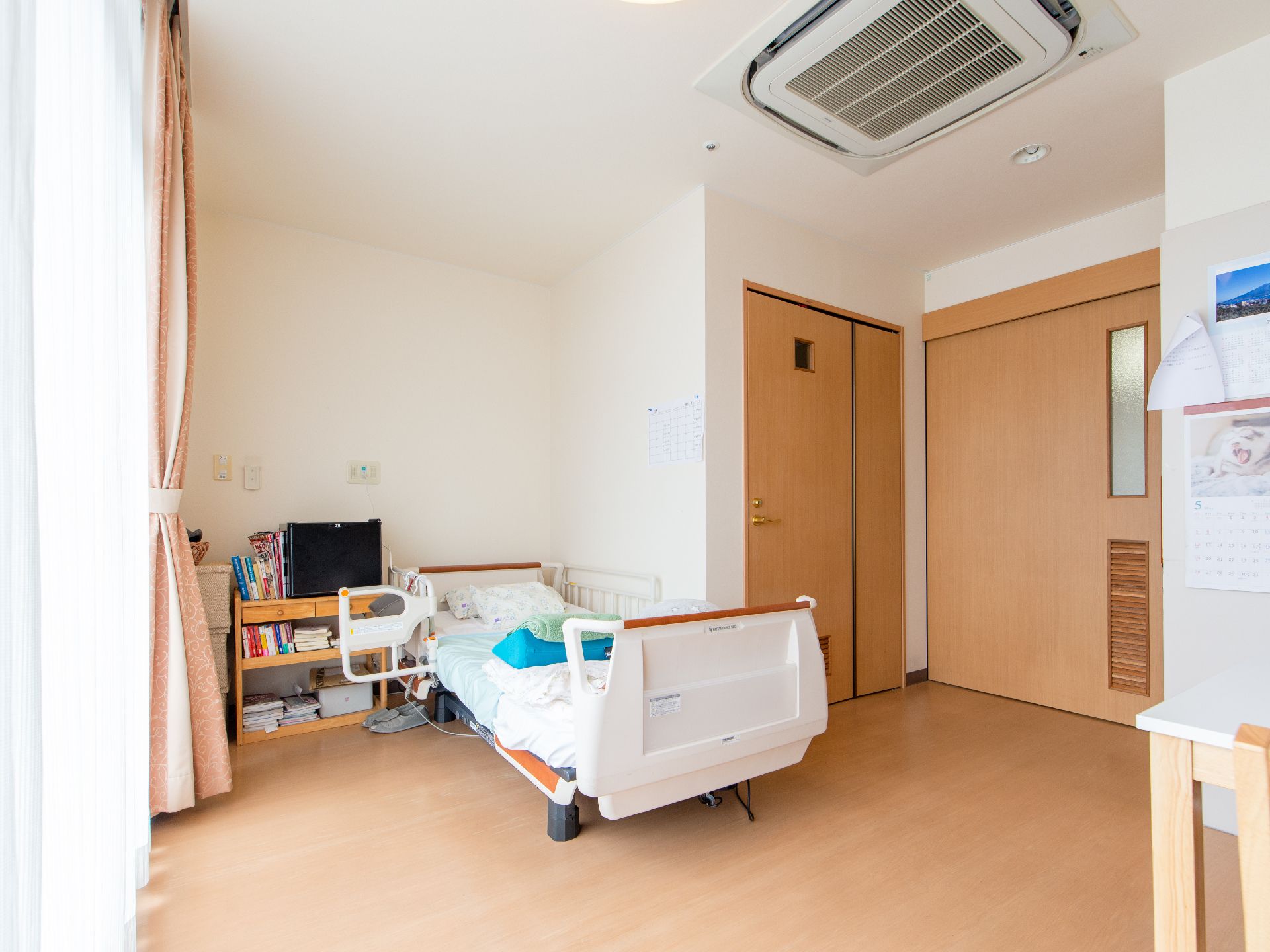 介護用ベッドや本棚などが置かれている明るい雰囲気の居室