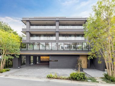 グレーの５階建ての建物。各フロアにベランダが付き、建物の周辺にはたくさんの木が植えられている。