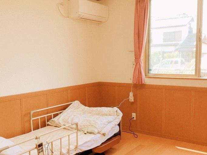 エアコンや介護用ベッドが置いてある小さなワンルームタイプの部屋。窓と緊急コールががある