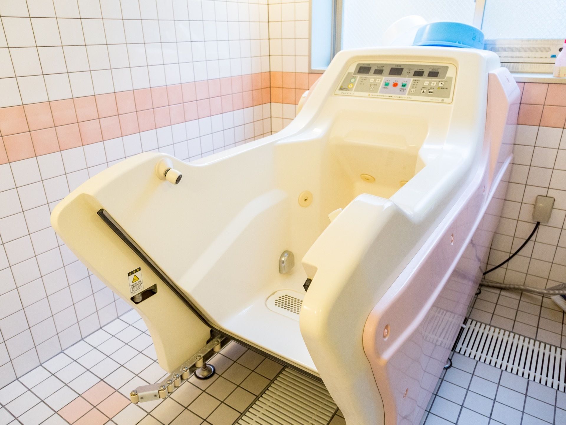 機械浴室は広く、介護機器が1台設置されている。上には水色の洗面器が置かれ、奥には窓も取りつけられている。