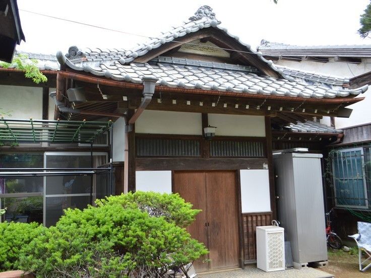瓦屋根の立派な日本家屋。折り畳み式のレジャーチェアや倉庫が置かれている。