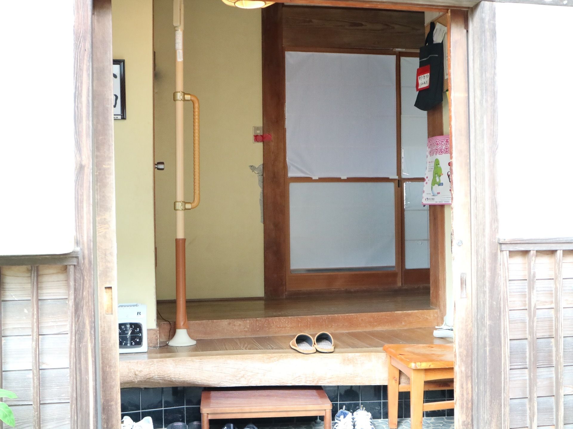 玄関の段差は高めのため、踏み台を設置している。手すりをつけている。昔ながらの家である。置き時計がある。