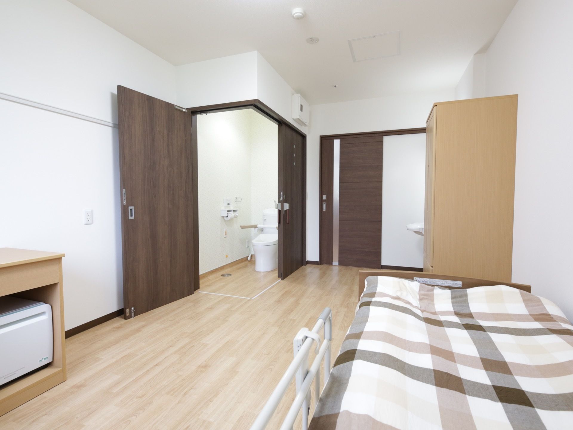 木目調のフローリングと白い壁に囲まれた、明るく広い室内である。扉がオープンになるトイレが設置されている。