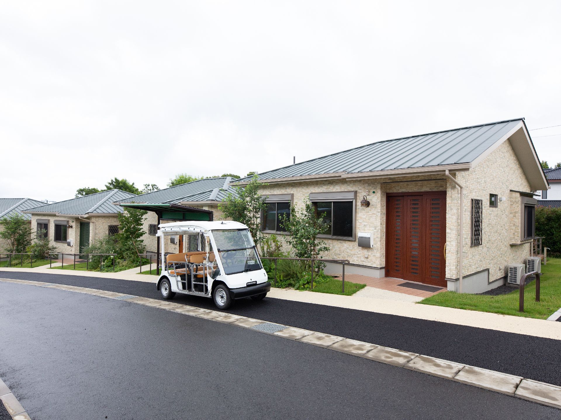 戸建て風の介護施設外観と、ドアのない個性的な白い車