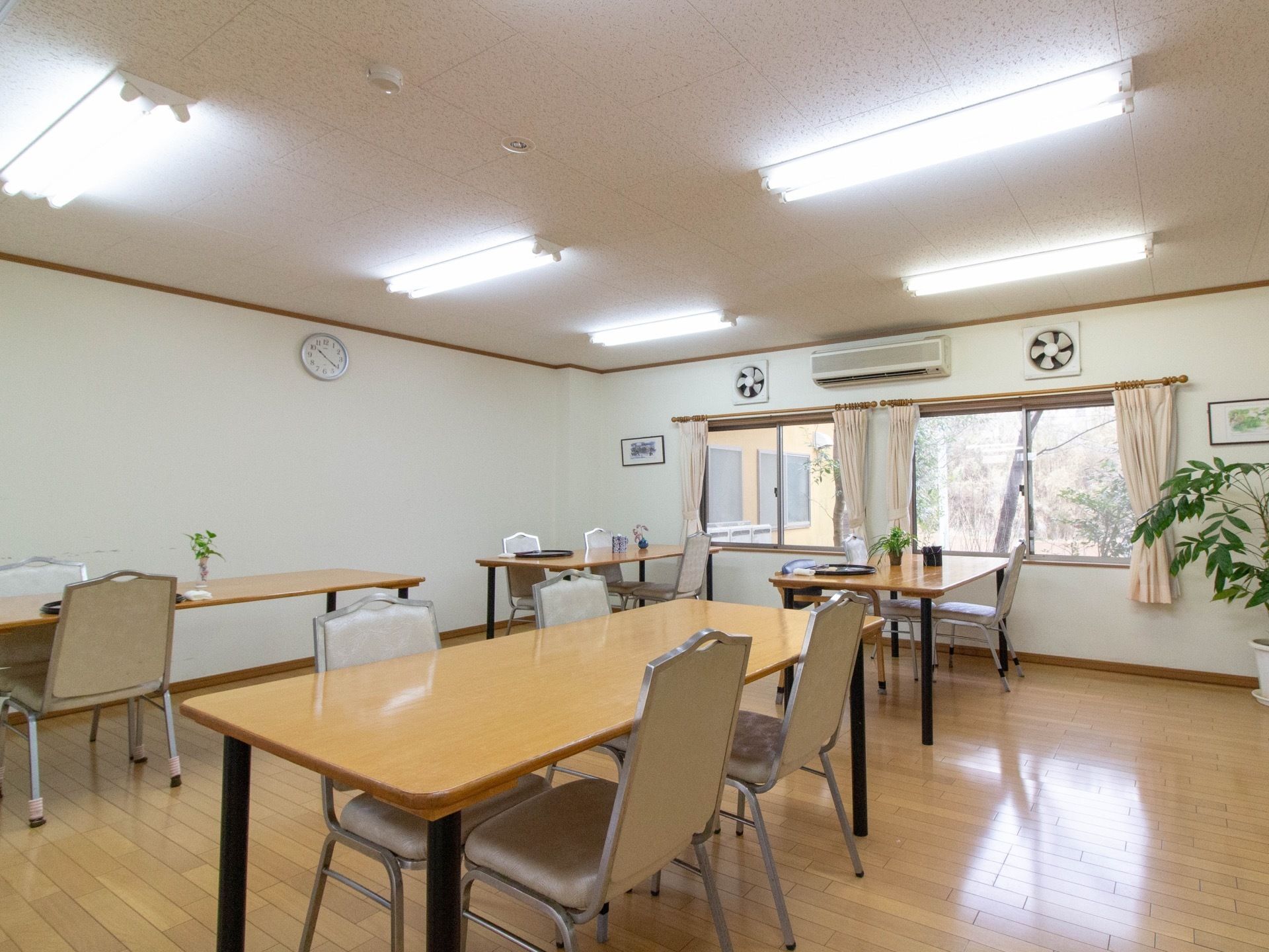窓から日射しが差し込む明るく広い食堂である。ダイニングテーブルは大きく、車椅子をご利用の方も着席できる。壁にエアコンが設置されている。