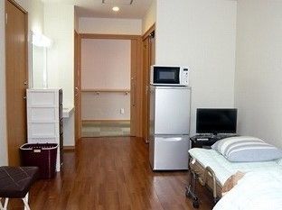 テレビや冷蔵庫、戸棚やベッドが写っている個室の様子。フローリング仕様の部屋の写真