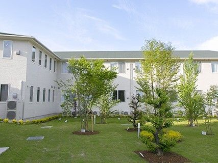 エル字型の建物は白い外壁で、ダークグレーの屋根が付いている。中庭は緑にあふれ、木もたくさん植えられている。