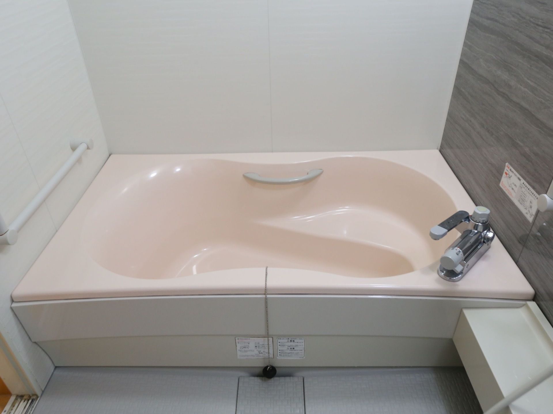一般家庭向けの浴槽で、浴槽内に腰がかけられる段差や手すりが設置されている。壁にも手すりがついている。