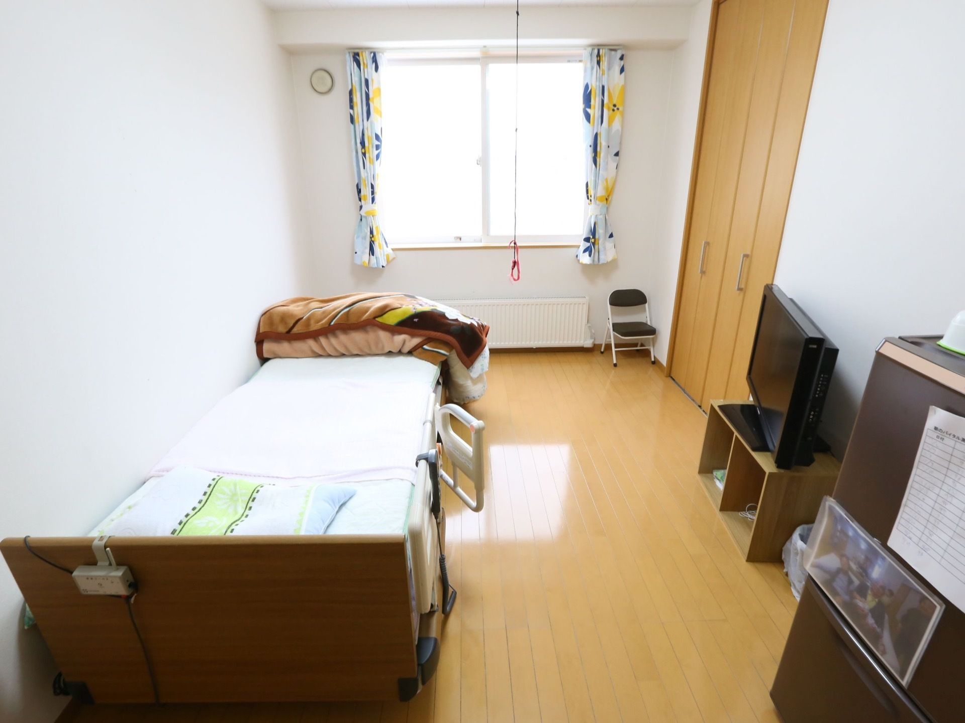 電動ベッドが壁に沿って置いてあり、正面の小さな台の上にテレビがある。その左側には、クローゼットが設置されている。