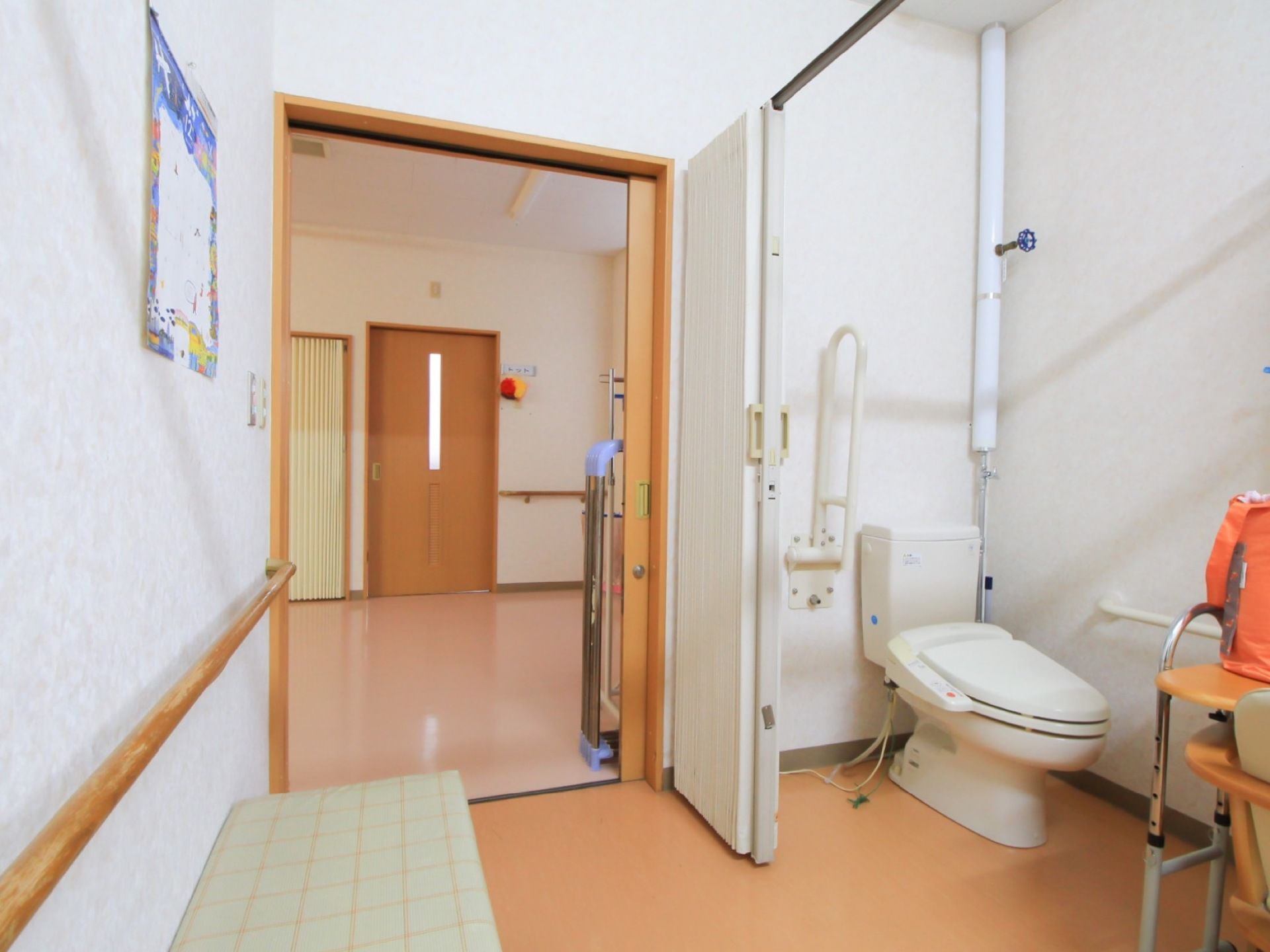 温水洗浄便座が採用されたトイレである。空間を仕切った形で設置されており、壁には手すりが取り付けられている。