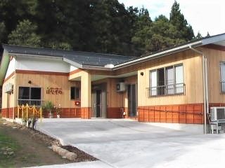 木造平屋建ての建物の外観写真。周辺を山に囲まれた自然部会場所