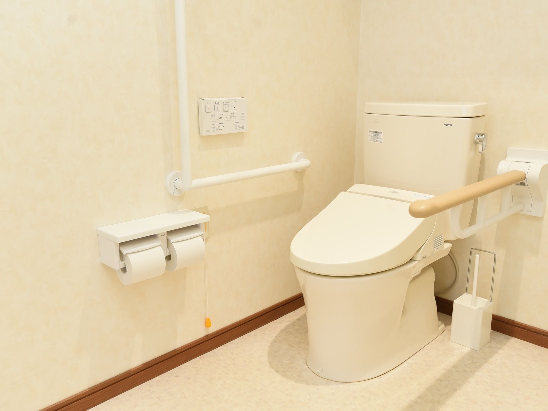 トイレは洋式タイプとなっている。右手側の壁にはＬ字型の手すりにナースコール、温水洗浄のコントーラーがある。