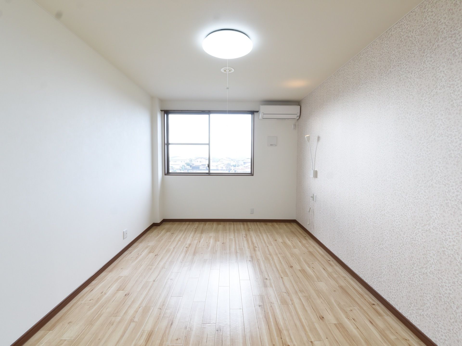 玄関ドア側から見た居室。ベッドサイドに当たる場所の壁には、支えの部分が自在に曲げられるライトが出ている。