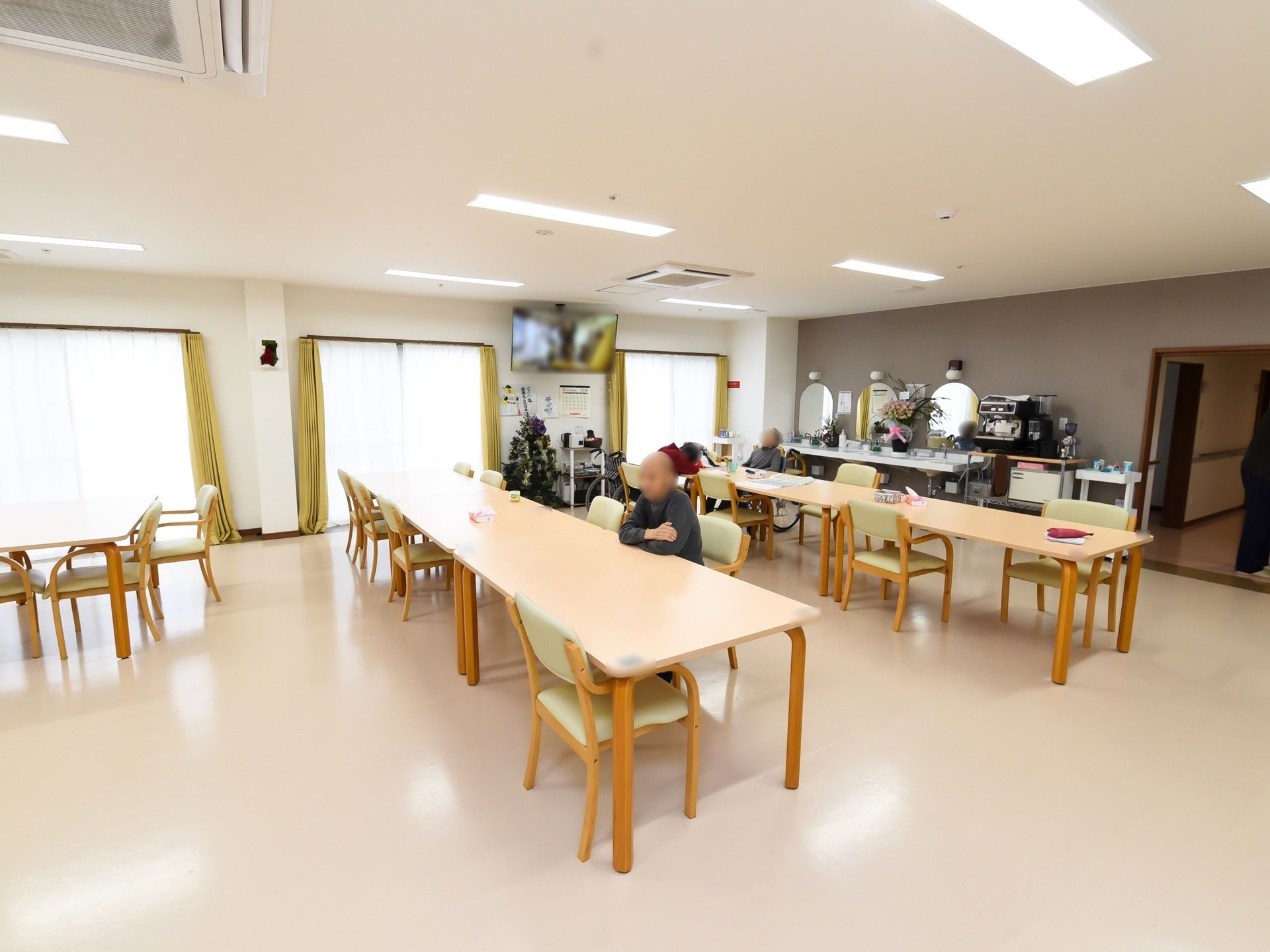 食堂とリビングを兼ねた広い共有スペース。天井には明るい照明の間に火災報知器、スプリンクラーなどが並んでいる。