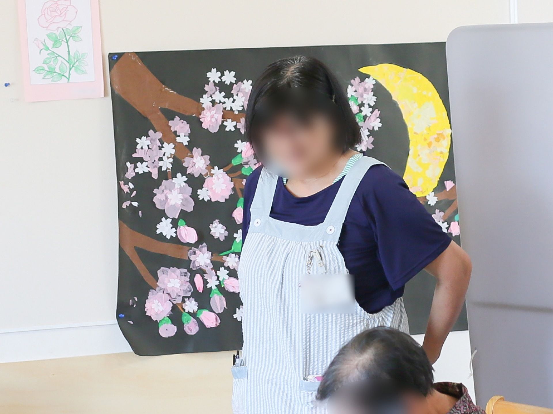 共有の空間にて入居者様の介護にあたるスタッフの様子。飾り気がなく動きやすい服の上からエプロンを着用している。