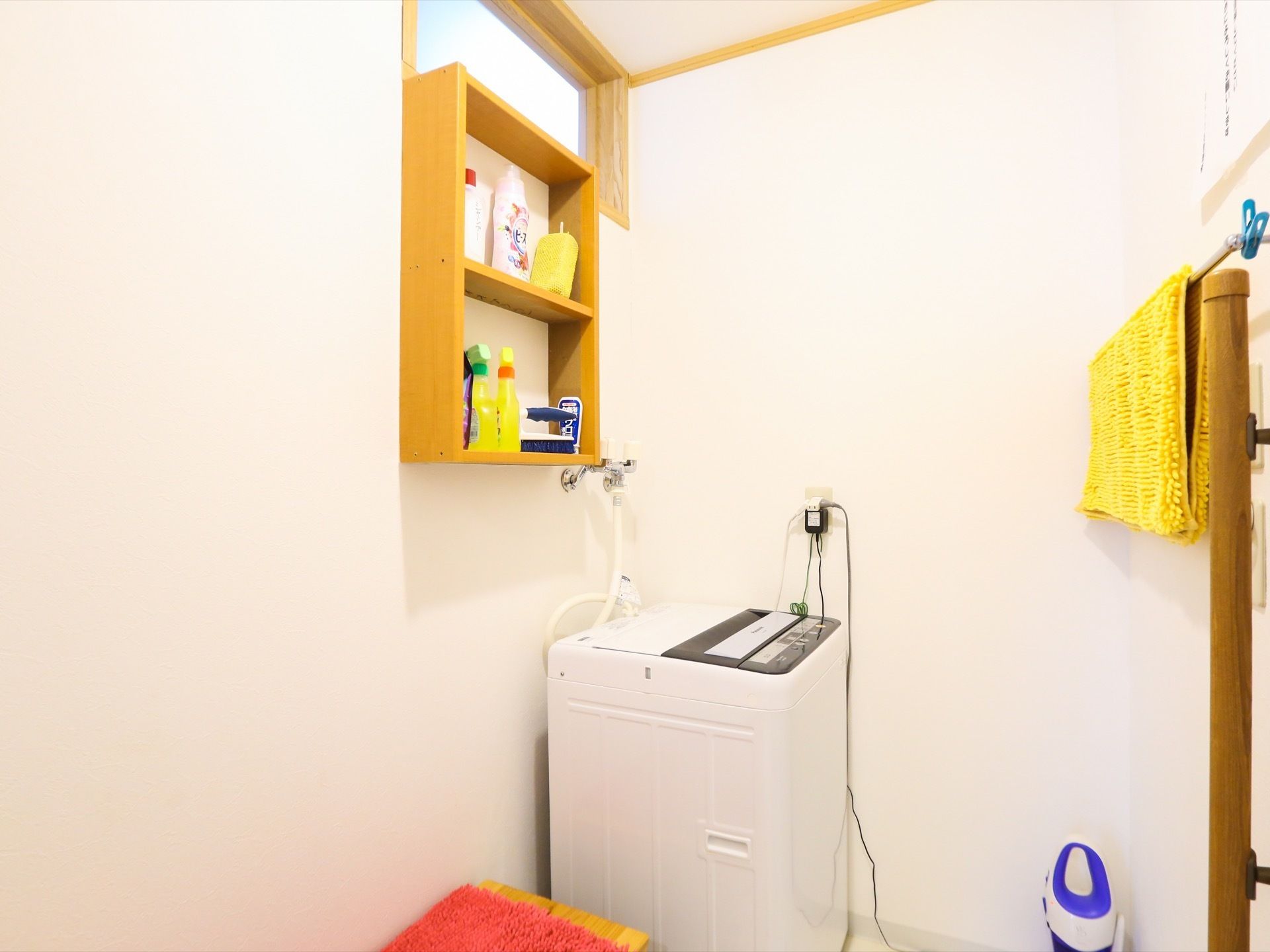 全自動の洗濯機である。そばには棚が作られており、洗剤などが置かれている。棚の上には木のフレームにおさまった窓がある。