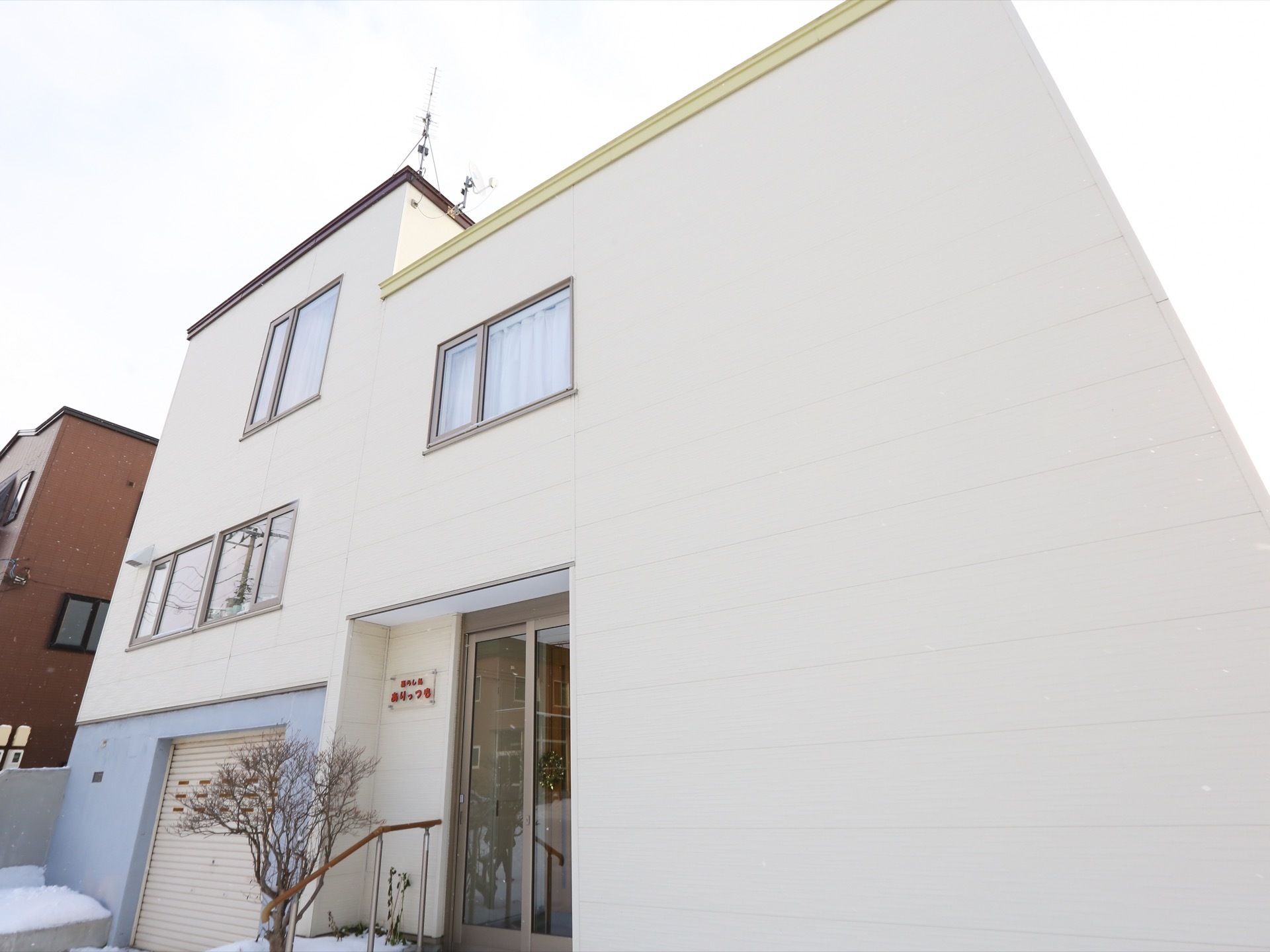 白い壁が印象的な外観である。玄関に向かって手すりが設置されている。屋根にはテレビのアンテナが備わっている。