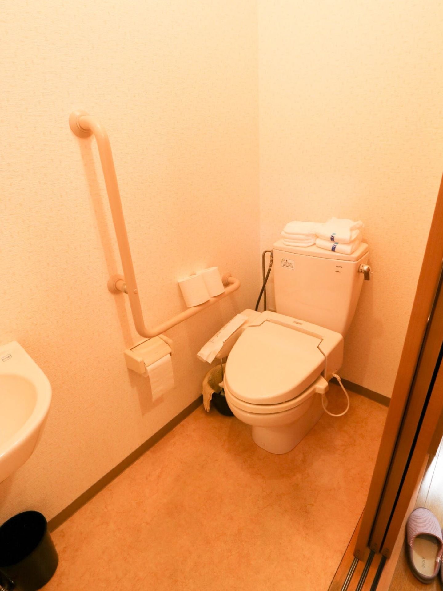 温水洗浄便座付きのトイレである。扉はスライドドアになっている。壁には手すりとペーパーホルダーが取り付けられている。