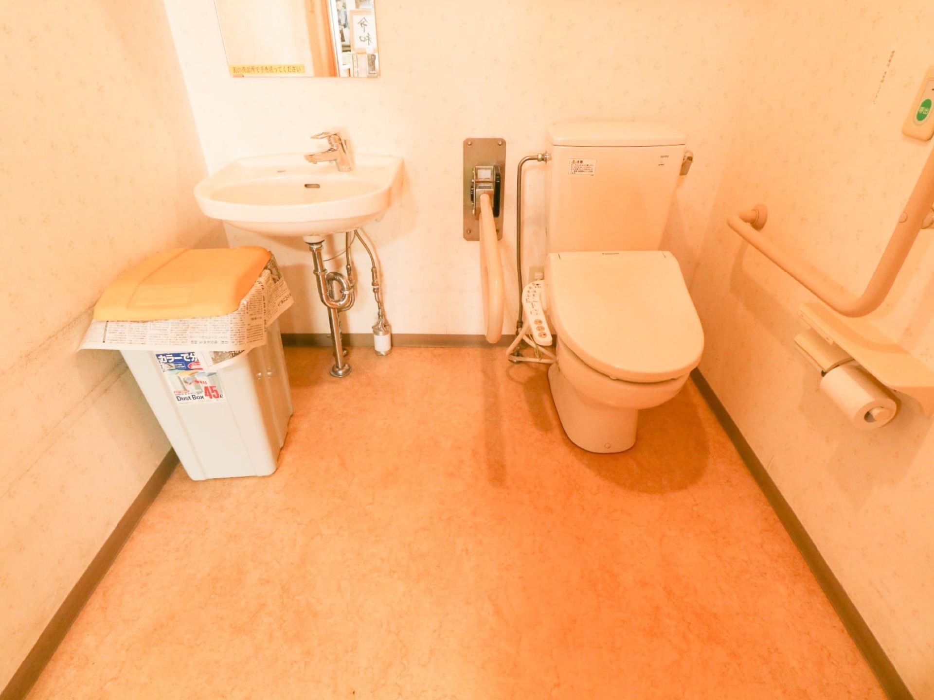 洗面台が併設されたトイレである。ゴミ箱が設置されており、壁には手すり、ペーパーホルダーが取り付けられている。