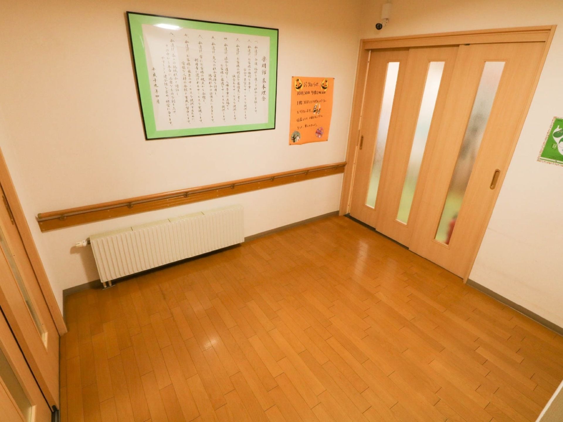 玄関に繋がる通路である。通路には暖房が設置されている。手すりが備わっており、壁には張り紙がされている。