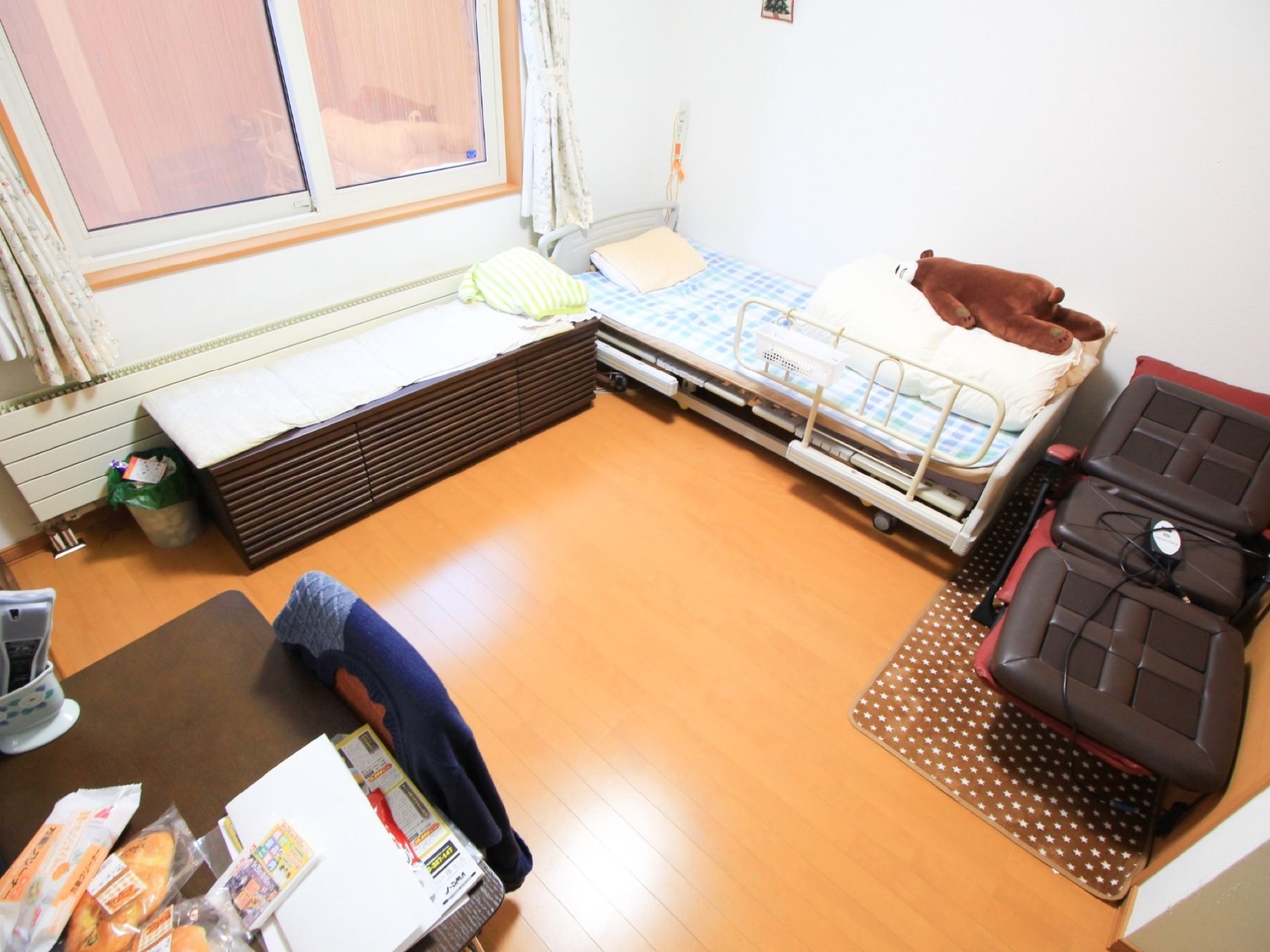 焦げ茶色のテーブルには、パンが3つ置いてあり、右側にリモコンがケースに入っている。椅子の上には、洋服が掛けてある。