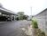 施設につながる道路である。のどかな雰囲気があり、道路の端に花が咲いている。玄関前のスペースに車が１台駐車している。