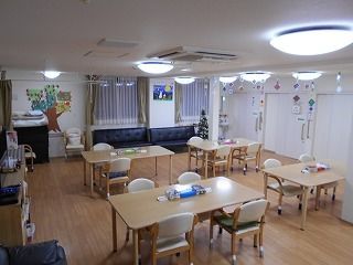 木製の4人掛けのダイニングテーブルが複数置かれ、手作りの装飾品が飾られたアットホームな雰囲気の食堂。