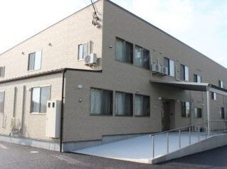 玄関には屋根があり、手すり付きのスロープがあるブラウン系の２階建ての建物は日当たりのいい場所にある。