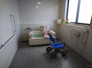 ブルーのシャワーチェアが置かれた浴室は洗い場が広く、奥には座ったまま入浴できる機械浴もある。